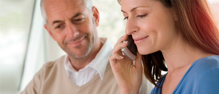 Frau telefoniert mit einem Lächeln, während ein Mann sie unterstützend ansieht.