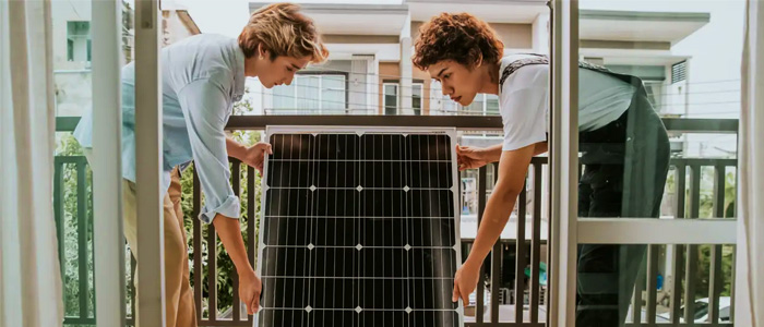Zwei Personen installieren gemeinsam ein Solarpanel auf einem Balkon.