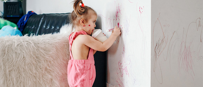 Kleines Kind malt mit Filzstiften an eine weiße Wand im Wohnzimmer.