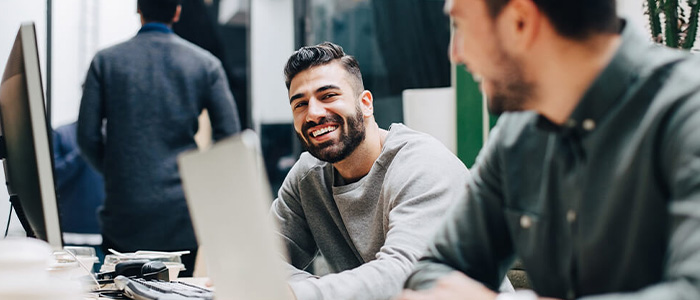 Zwei Kollegen unterhalten sich lachend im modernen Büro am Arbeitsplatz.
