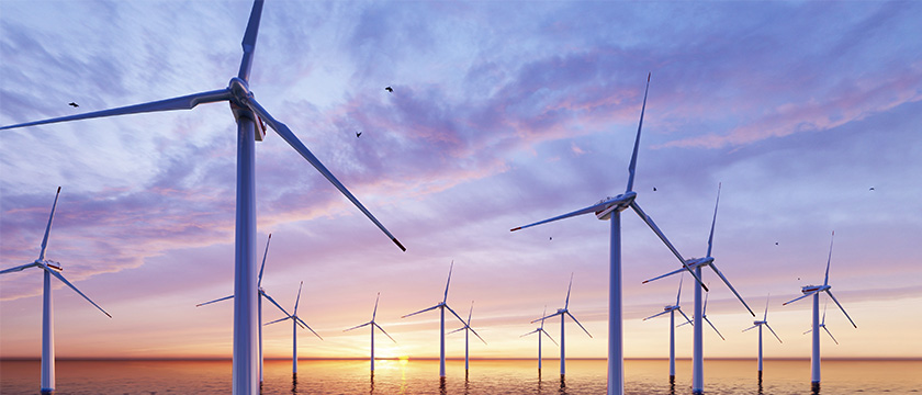 Windräder im Meer bei Sonnenuntergang mit farbenfrohem Himmel.
