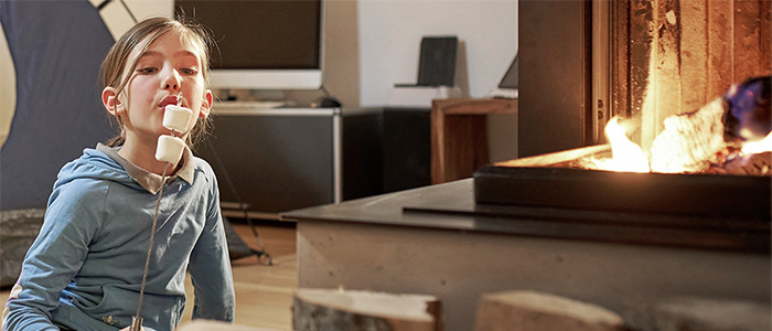 Mädchen röstet Marshmallows am Kaminfeuer im Wohnzimmer.